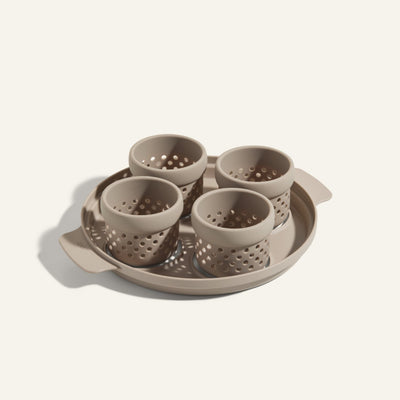 The Egg Poacher includes a beige tray and four matching perforated silicone cups, ideal for poaching eggs, all crafted from the same material and displayed against a light background.