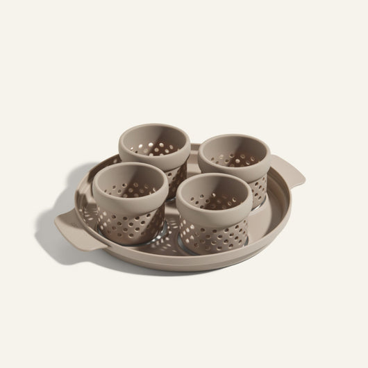 The Egg Poacher includes a beige tray and four matching perforated silicone cups, ideal for poaching eggs, all crafted from the same material and displayed against a light background.