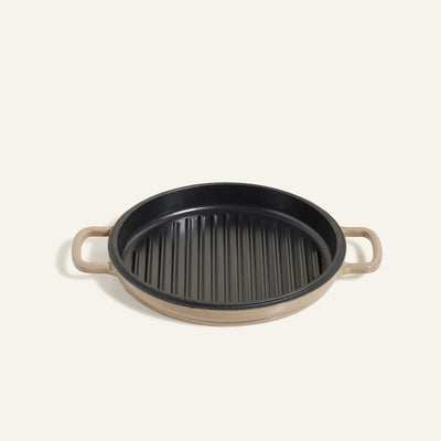 The Cast Iron Hot Grill is a round grill pan with a beige handle and black ridged surface, shown from above on a light background.