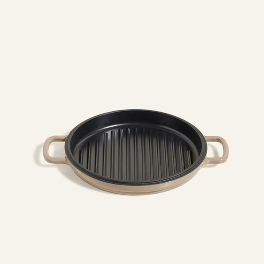 The Cast Iron Hot Grill is a round grill pan with a beige handle and black ridged surface, shown from above on a light background.