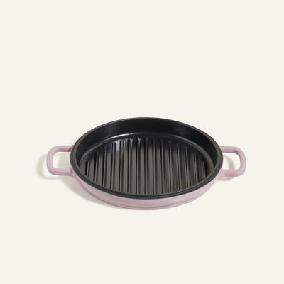 The Cast Iron Hot Grill is a round, purple premium grill pan with black ridges and two handles, crafted from enameled cast iron, displayed against a plain light background.