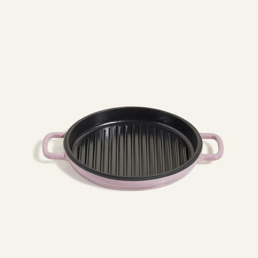 The Cast Iron Hot Grill is a round, purple premium grill pan with black ridges and two handles, crafted from enameled cast iron, displayed against a plain light background.