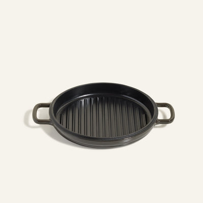 The Cast Iron Hot Grill is a round, black enameled cast iron pan with two side handles and a ridged surface—ideal as a premium grill pan for all your indoor grilling needs.