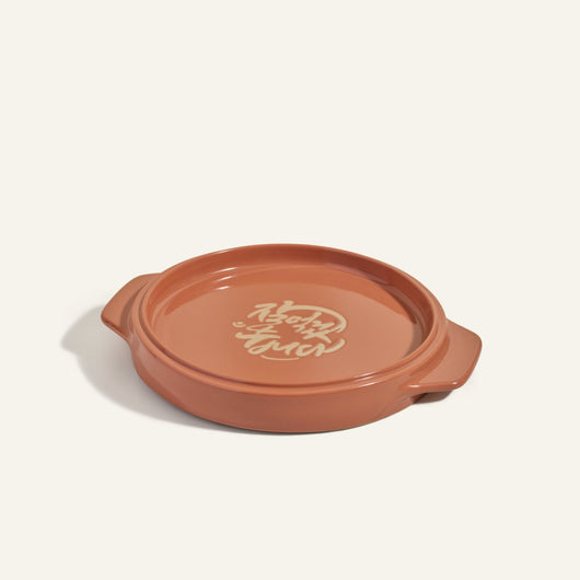 The Flipping Platter is a round, brown ceramic dish with side handles and Korean script on its flat base, ideal for serving tahdig or as a tray to flip maqluba.