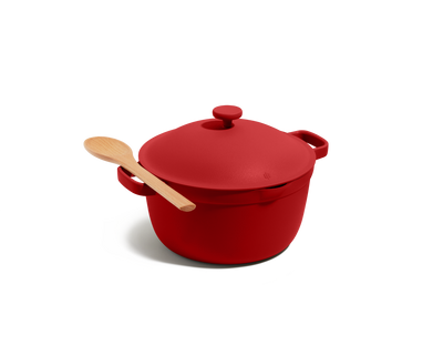 The Perfect Pot, a red family-sized Dutch oven with a matching lid and a wooden spoon on top, set against a plain white background.