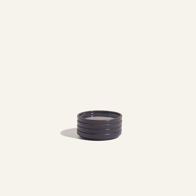A stack of four Tiny Plates—small, round ceramic snack plates—rests on a light, plain background, perfect for any tableware set.