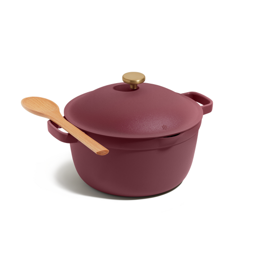 The Perfect Pot, a maroon cast iron Dutch oven with a gold knob, is displayed on a white background with a wooden spoon resting on its lid. This versatile pot is ideal for family meals.