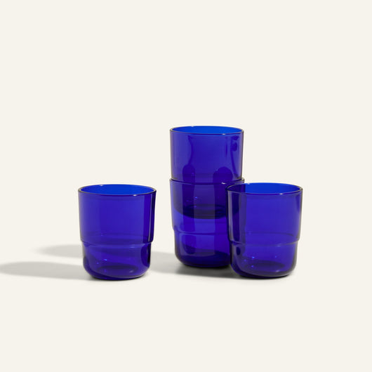 Four Short Night + Day Glasses in cobalt blue recycled glass are stacked on a neutral background, highlighting vibrant drinking tumblers ideal for any table setting.