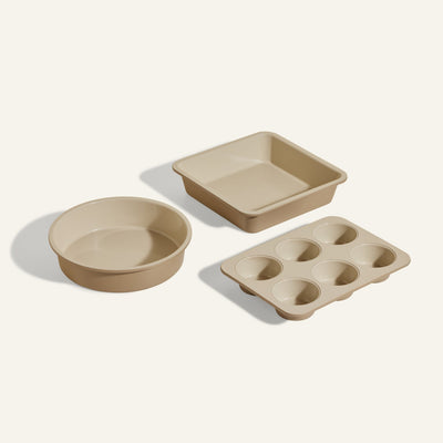 The Wonder Oven Baker’s Kit includes three beige non-toxic pans—a round cake pan, a square cake pan, and a six-cup muffin tin—arranged on a light background, perfect for your Wonder Oven baking needs.