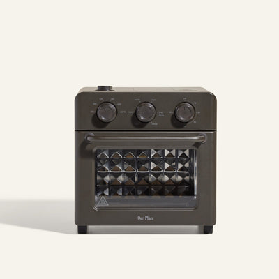 The AU - Wonder Oven is a dark gray countertop toaster oven with three top control dials and a front glass door featuring a diamond-patterned interior. "Our Place" appears at the bottom of the door. Doubles as an air fryer for extra versatility.