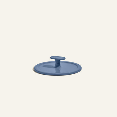 A blue, round cast iron Grill Press with a central handle is shown on a plain off-white background, perfect for even heat distribution.