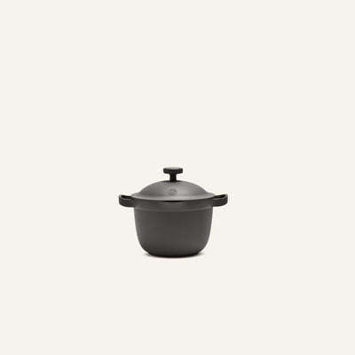 The Petite Perfect Pot, a black cast iron pot with two side handles and a lid, is centered against a plain light background.