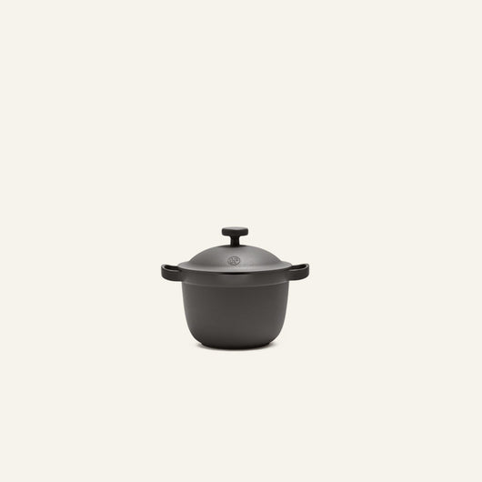 The Petite Perfect Pot, a black cast iron pot with two side handles and a lid, is centered against a plain light background.