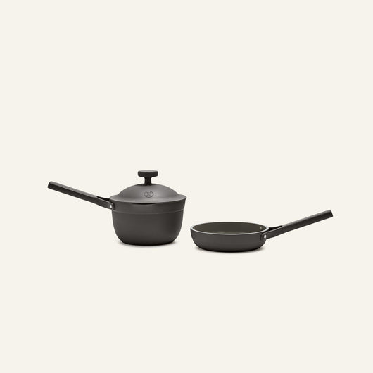 The Tiny Cookware Duo, featuring a black saucepan with lid and a matching black frying pan, are placed side by side against a plain light background.