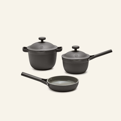 The Tiny Cookware Duo + Petite Perfect Pot set features a matte gray lidded pot, a lidded saucepan, and a frying pan with black handles, showcased on a simple light background.