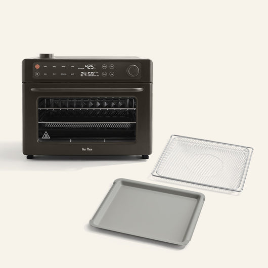 The Wonder Oven Pro + Wonder Oven Pro Essentials Kit is a black countertop air fryer oven with a digital display, shown with a wire rack and baking tray in front of it on a light background.