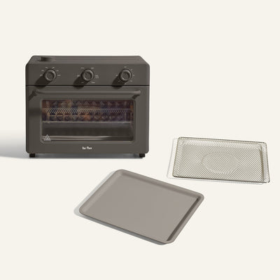 The Large Wonder Oven + Large Wonder Oven Essentials Kit is displayed in black, with a wire rack and baking tray placed in front of it against a simple background.