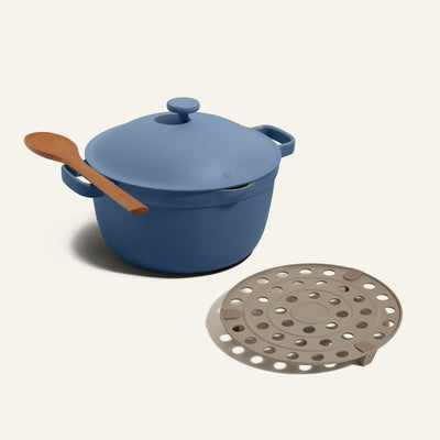 The Perfect Pot with Roasting Rack features a blue pot with a lid and a wooden spoon on its handle, alongside a round beige steamer insert with holes.