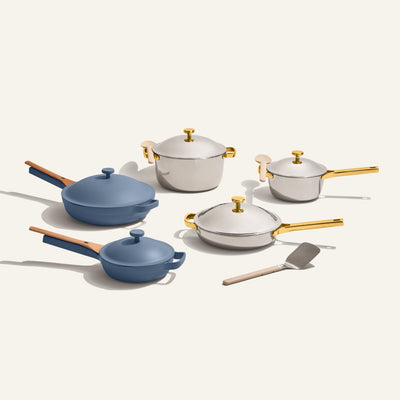 The Home Chef Set (15 piece) features blue and white ceramic cookware with gold or wood handles and a metal spatula, all elegantly arranged on a light background.