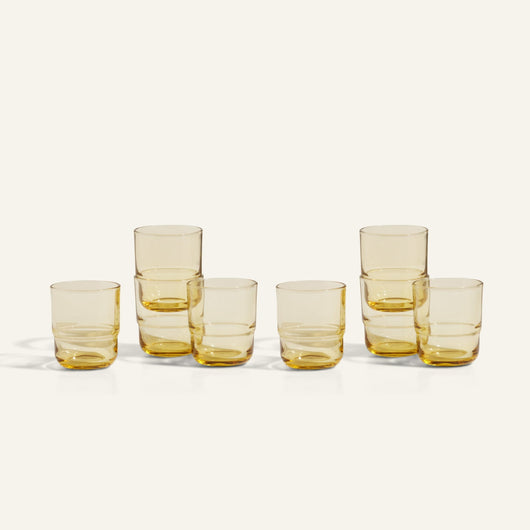 Six amber-tinted Short Night + Day Glasses, handcrafted from recycled glass, are arranged in two rows on a light background—some stacked—showcasing their artisanal charm.