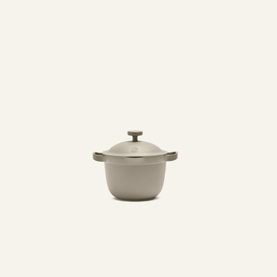 A beige Petite Perfect Pot with two side handles and a knobbed lid is centered on a plain off-white background.
