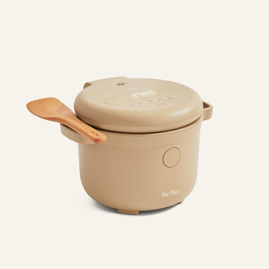 Beige Rice Cooker with fuzzy logic, digital display, closed lid, and wooden spatula on the handle; "Our Place" brand printed on front—makes perfect rice every time.