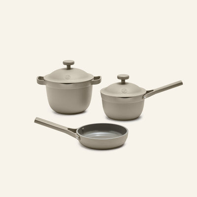 The Tiny Cookware Duo + Petite Perfect Pot set, featuring a pot, saucepan, and frying pan with matching lids and handles in beige, is displayed on a neutral background.