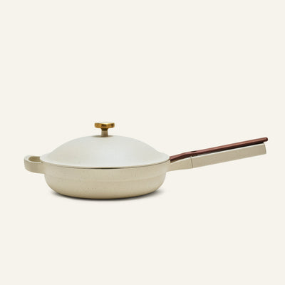 The non toxic ceramic nonstick always pan 2.0, a beige nonstick frying pan from a bestselling cookware set, comes with a matching domed lid, wooden handle, and brass knob, shown against a plain light background.